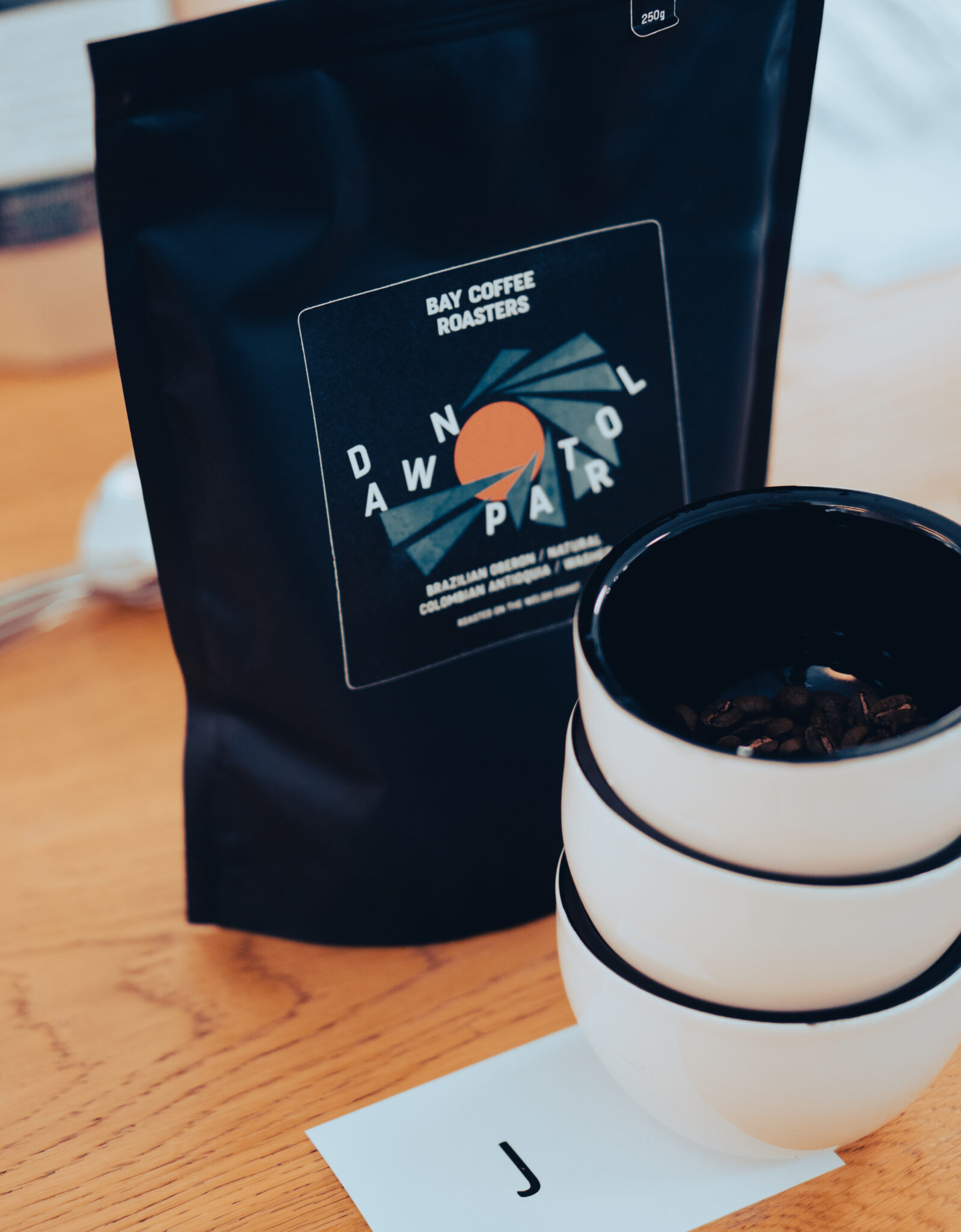 A bag of roasted coffee beans next to a few cups ready to be tasted