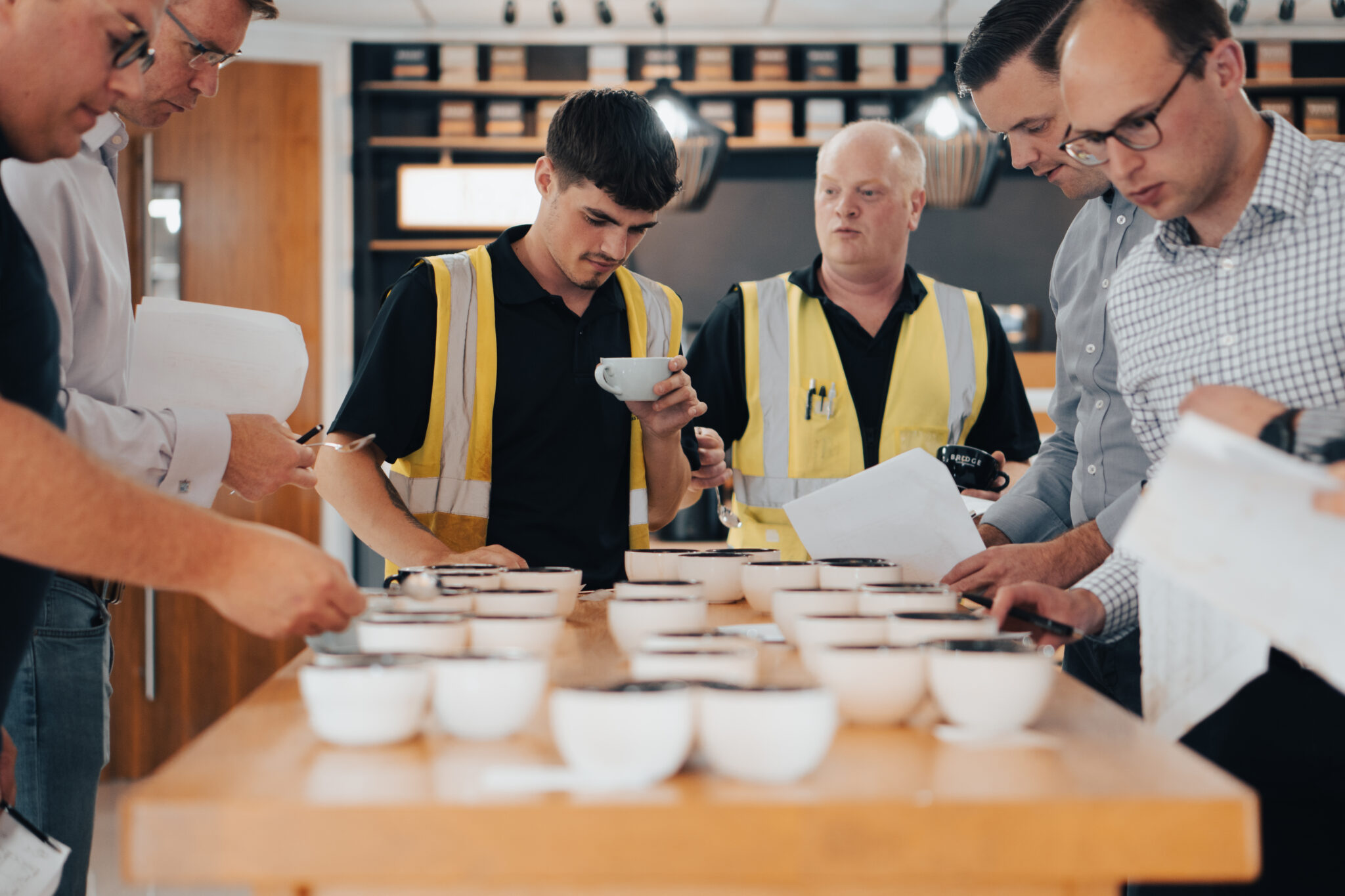 Six staff members gathered around a table tasting different cups of coffee